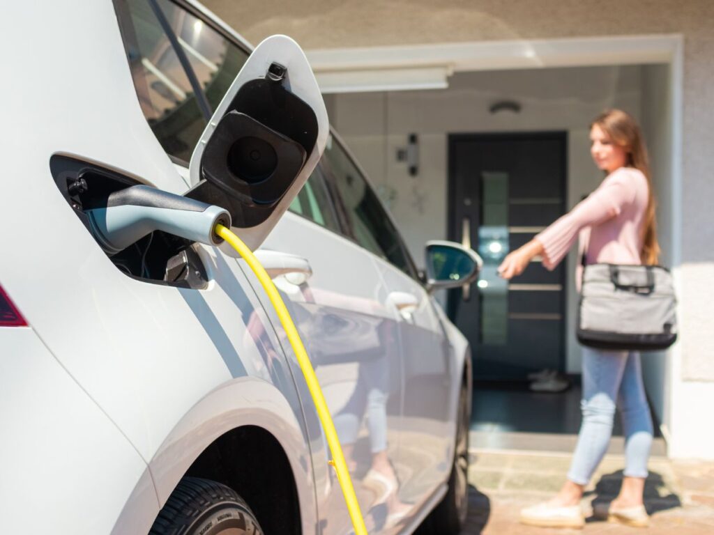 woman standing outside a white sedan with an EV charger plugged into it